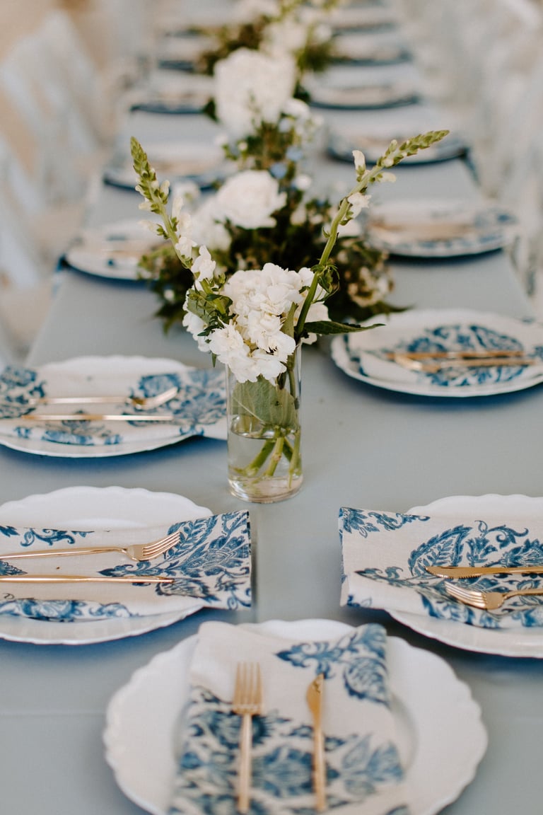 Elegant table setting with blue patterned plates and floral centerpieces, perfect for a wedding or formal event.