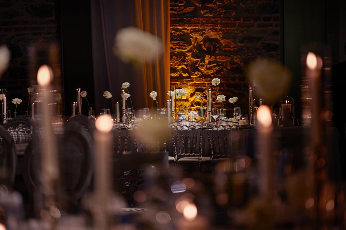 Romantic wedding reception scene featuring elegant tables adorned with white flowers, glassware, and tall candles inside a historic stone venue.