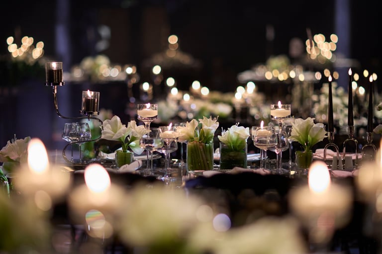 Elegant banquet tables illuminated by candlelight, featuring refined floral centerpieces and carefully arranged table settings in a luxury event environment.